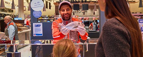 Ein Mitarbeiter zeigt Kund:innen einen frischen Fisch von der INTERSPAR-Fischtheke