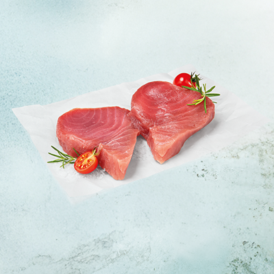 Zwei frische Thunfischfilets neben halbierten Cocktailtomaten auf einem hellen Stück Papier