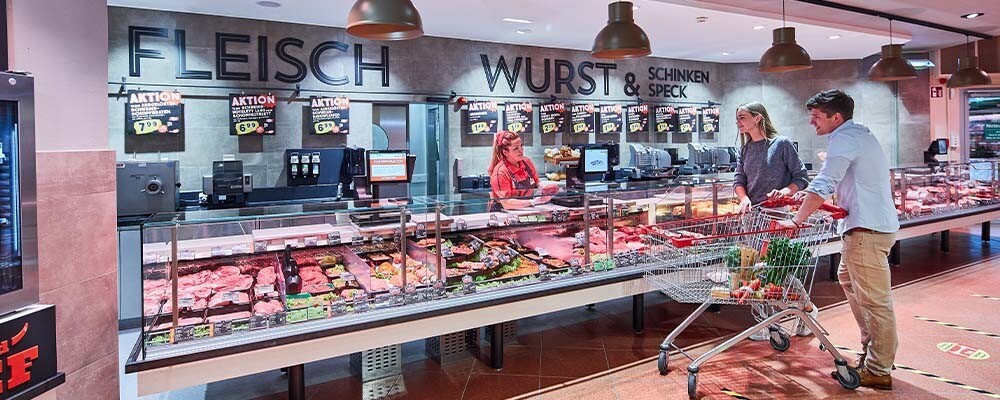 Zwei Personen mit einem Einkaufswagen an einer Fleischtheke