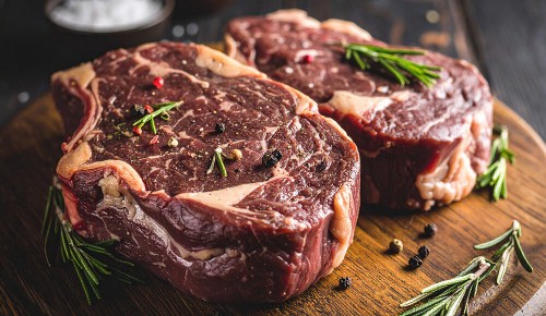 Zwei Stücke Dry Aged Beef garniert mit Rosmarinzweigen auf einem Holzbrettchen