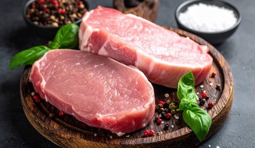 Zwei Stücke Schweinefilet garniert mit Basilikumblättern auf einem Holzbrettchen