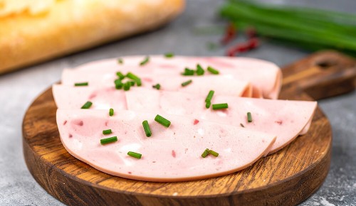 Mehrere Scheiben Wurst garniert mit Schnittlauch auf einem Holzbrettchen