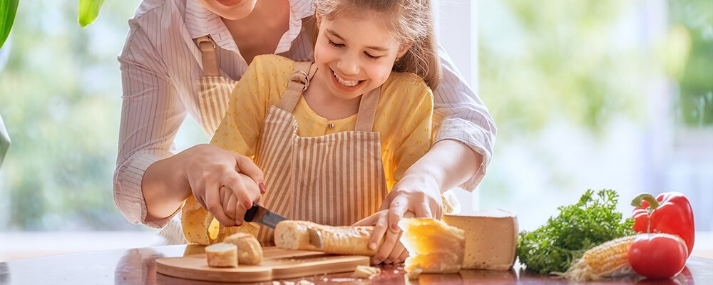 Eine Frau und ein kleines Mädchen schneiden gemeinsam Brot auf einem Brettchen