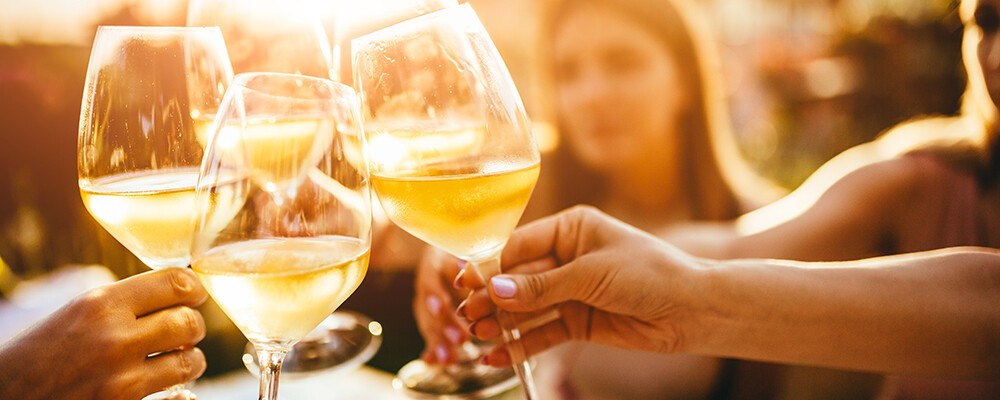 Mehrere Personen, die auf der Sommerterrasse eines Cafés mit Weingläsern anstoßen 