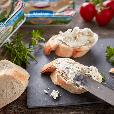 Frischkäse wird mit einem Messer auf einem Stück Baguette verstrichen