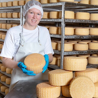 Eine Mitarbeiterin der Rotholz Käserei mit einem Laib Käse in den Händen