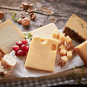 Verschiedene Stücke Hartkäse mit Nüssen und Weintrauben auf einem Holztisch