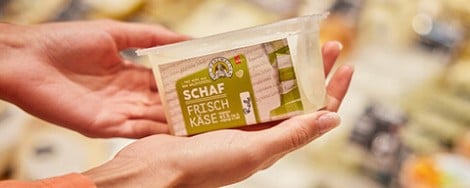 Eine  Person hält eine Verpackung Ziegen-Frischkäse in der Hand