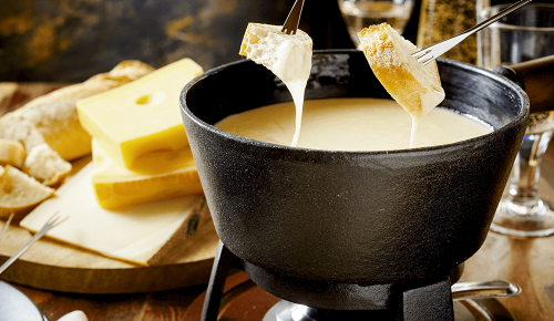 Stücke Brot werden mit Fondue-Spießen in ein Käsefondue getunkt