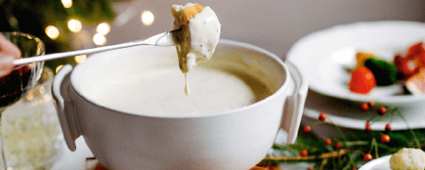 Ein Stück Weißbrot wird mit einem Fondue-Spieß in ein Käsefondue getunkt