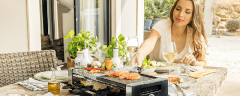 Eine Frau grillt verschiedenes Obst und Gemüse auf einem Raclette-Grill