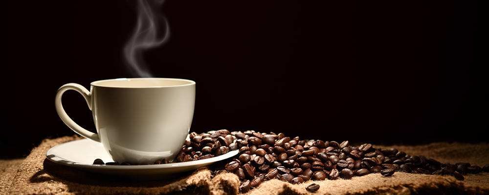 Dampfender Kaffee in weißer Tasse neben Kaffeebohnen auf Jutesack
