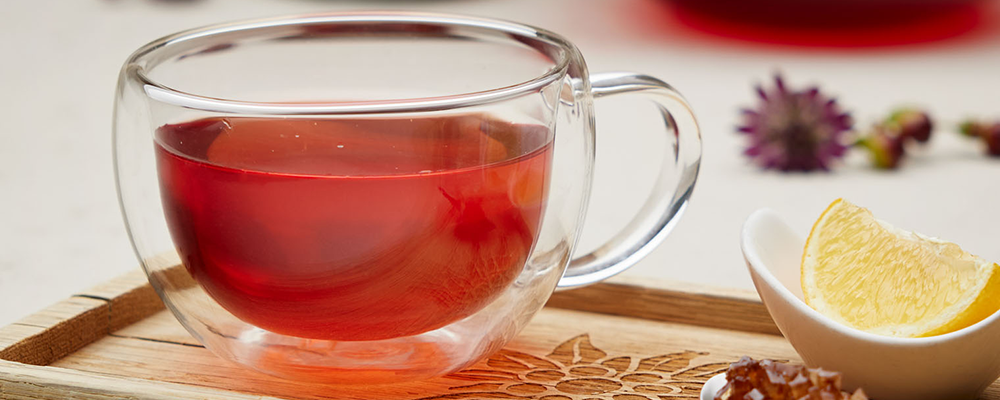 Eine Teetasse aus Glas mit rotem Früchtetee auf einem Holztablett