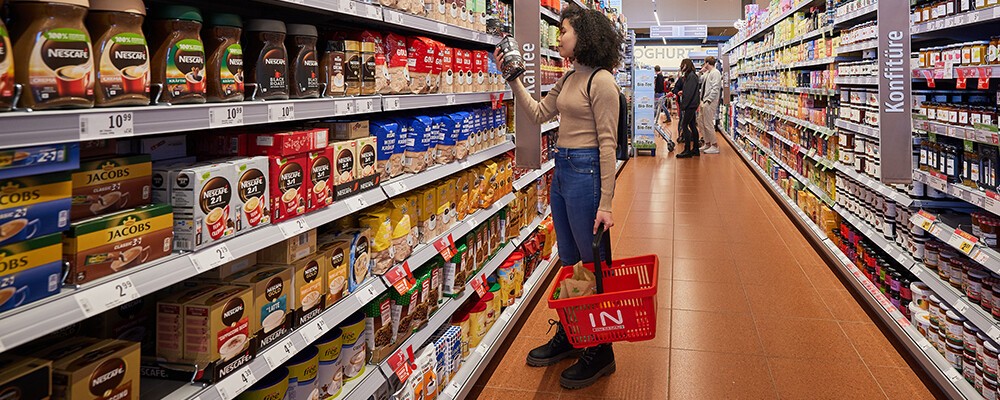 Eine Frau mit einem Einkaufskorb beim Ansehen von Kaffee-Produkten in einem INTERSPAR