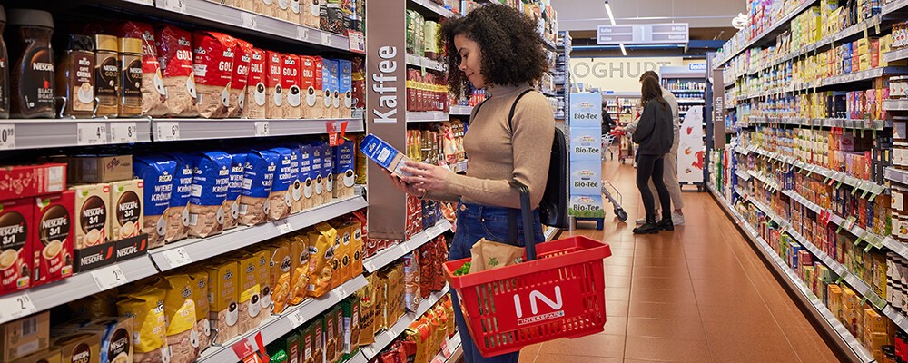 Eine Frau mit einem Einkaufskorb beim Ansehen von Kaffee-Produkten in einem INTERSPAR