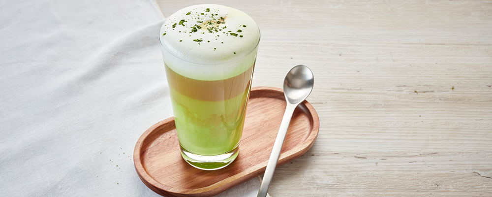 Ein Latteglas mit Matcha Latte auf einem kleinen Holztablett