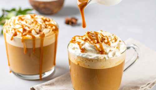 Zwei Tassen mit Caramel-Latte auf den eigen gerade Karamell gegossen wird
