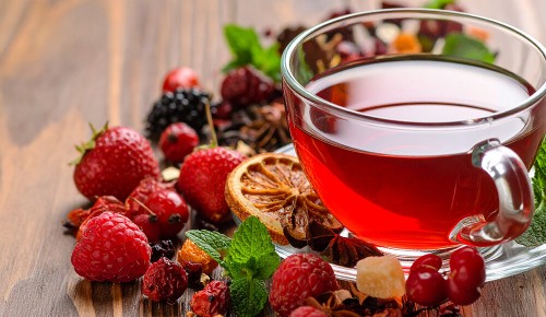 Eine Glastasse mit rotem Früchtetee neben verschiedenen Beeren