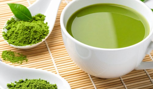 Eine Tasse grüner Tee neben einem Porzellan-Löffel mit Matcha-Pulver