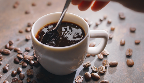 Tasse Americano-Kaffee und geröstete Kaffeebohnen neben der Tasse auf einem Holztisch. Ansicht von oben.