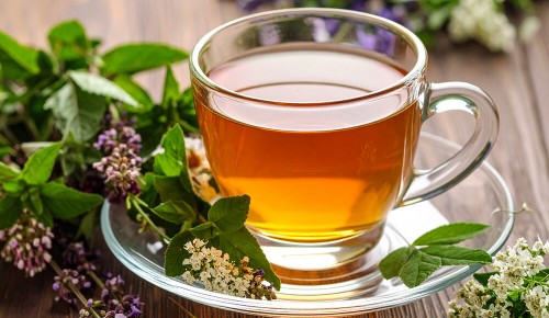 Eine Tasse Kräutertee neben verschiedenen frischen Kräutern