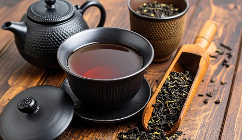 Eine schwarze Tasse mit frischem Oolong-Tee neben einer schwarzen Teekanne