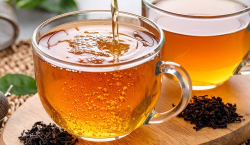 Zwei Glastassen mit frischem Schwarztee neben getrockneten Teeblättern