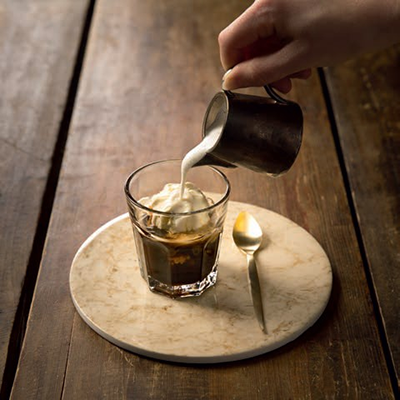 Eine Person gießt etwas Milch auf einen Affogato in einem Gläschen
