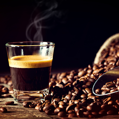 Espresso in einem Glas, daneben Kaffeebohnen