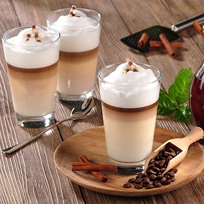 Drei Café Latte in Gläsern auf einem Tisch mit Zimtstangen und Bohnen
