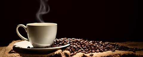 Dampfender Kaffee in weißer Tasse neben Kaffeebohnen auf Jutesack