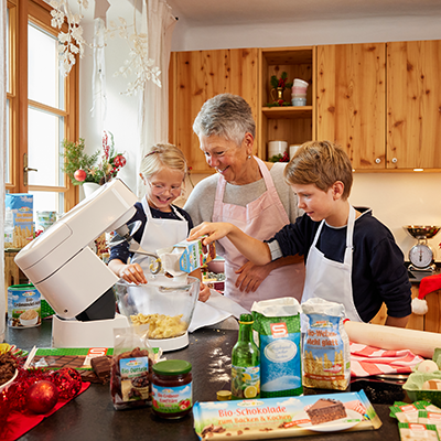 Eine ältere Frau backt gemeinsam mit zwei Kindern in einer Küche
