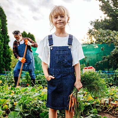 Ein kleines Mädchen in Gartenkleidung mit Karotten in der Hand in einem Feld
