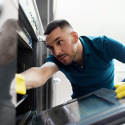 Ein Mann beim Putzen eines Backrohrs mit gelben Handschuhen