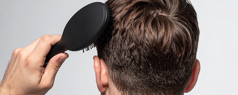 Braune Haare werden mit einer schwarzen Bürste gekämmt.