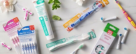 Verschiedenste Zahnpflege-Produkte mit Blüten und Blättern auf Fliese.