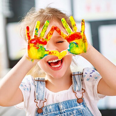 Ein lachendes kleines Mädchen mit bunt angemalten Händen 