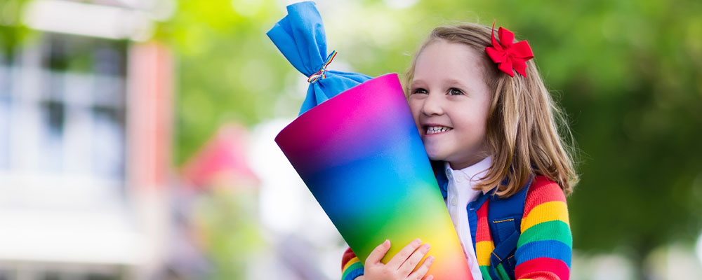 Ein kleines Mädchen hält eine regenbogenfarbene Schultüte in der Hand