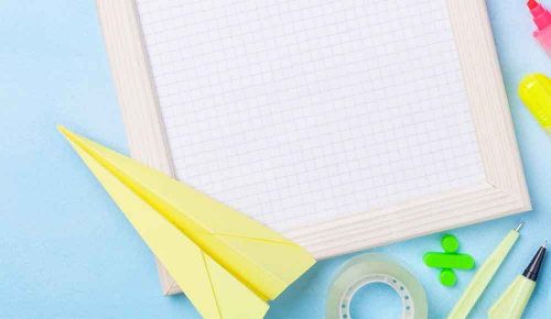 Ein gelber Papierflieger und ein karierter Notizblock