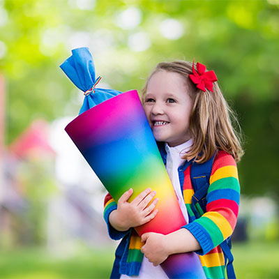 Ein kleines Mädchen hält eine regenbogenfarbene Schultüte in der Hand