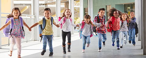 Viele kleine Schulkinder laufen mit Schultaschen durch einen Gang