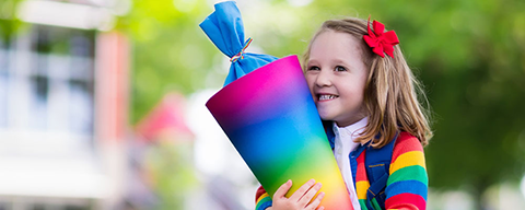 Ein kleines Mädchen hält eine regenbogenfarbene Schultüte in der Hand