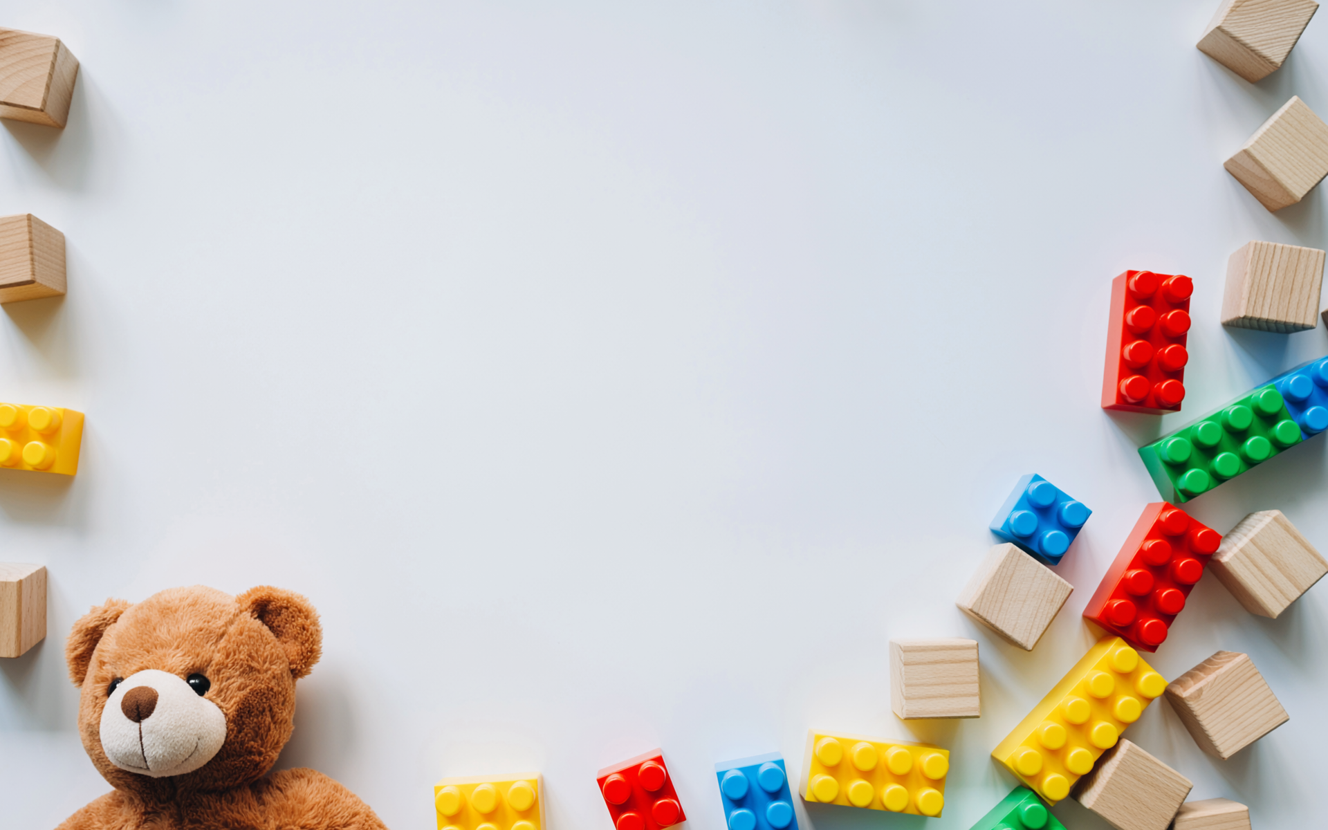 Verschiedene Spielsachen wie Legosteine, Bauklötze und ein Teddybär auf einem weißen Untergrund