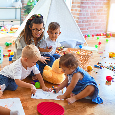 Mehrere Kinder mit einer Frau spielen und zeichnen am Boden