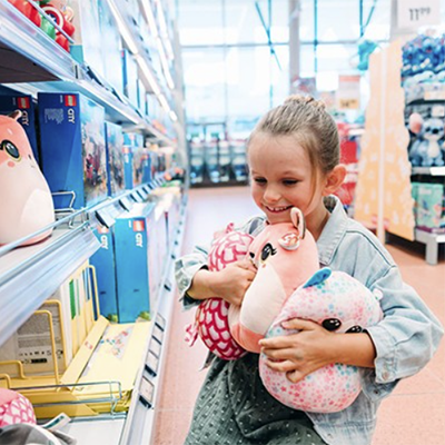 Ein kleines Mädchen steht mit verschiedenen Kuscheltieren in den Armen in einem INTERSPAR-Hypermarkt