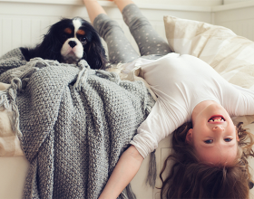 Ein Mädchen liegt verkehrt herum neben einem Hund auf dem Bett