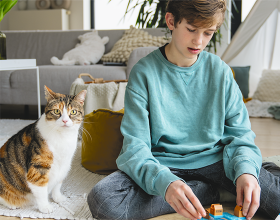 Ein Junge sitzt spielend neben einer Katze auf dem Boden