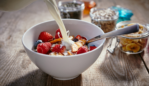 Eine Milchalternative wird ein eine Schale Müsli mit frischen Beeren gegossen