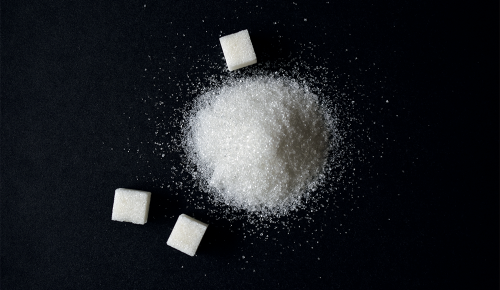 Zuckerwürfel und ein Häufchen Zucker auf einem schwarzen Tisch