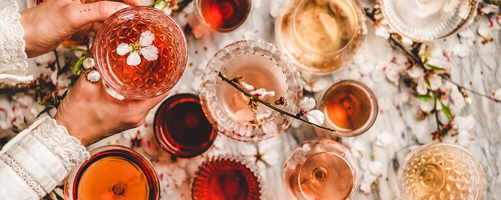 Eine Frau hält ein Glas Roséwein in der Hand, im Hintergrund viele verschiedene Weingläser